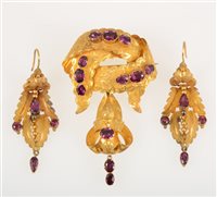 Lot 265 - A Victorian yellow metal brooch and earrings suite set with almandine garnets, ribbon design with dropper to base, total gross weight approximately 13.8gms. (3)