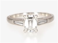 Lot 174 - A diamond solitaire ring, the emerald cut stone four claw set in a platinum mount with a tapered baguette cut diamond set into each shoulder