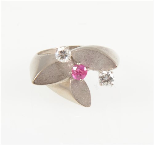 Lot 221 - A contemporary ruby and diamond dress ring, two brilliant cut diamonds and a single pink ruby claw set on a white metal floral mount with three satin finish petals, shank marked 585