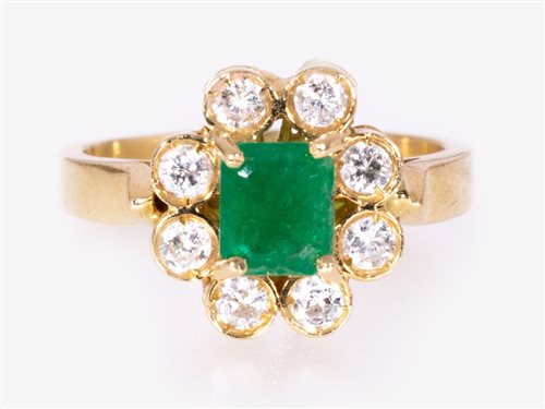 Lot 244 - An emerald and diamond oval cluster ring, the rectangular step cut emerald four claw set and surrounded by eight brilliant cut diamonds in an all yellow metal mount marked 750, ring size I.