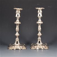 Lot 173 - Pair of George II style silver-plated on copper candlesticks, shaped square removable sconces with shell fluting, on knopped and waisted columns