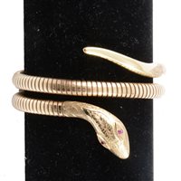 Lot 191 - A 9 carat yellow gold snake bangle, 6mm coiled snake link terminating in a snakes head set with ruby eyes