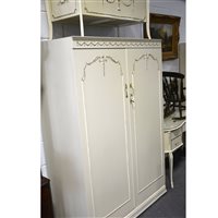 Lot 453 - Cream and gilt five-piece melamine bedroom suite, comprising kidney shaped dressing table, triptych mirrors over, width 130cm; two two-door wardrobes; a nest of five drawers and an ottoman.