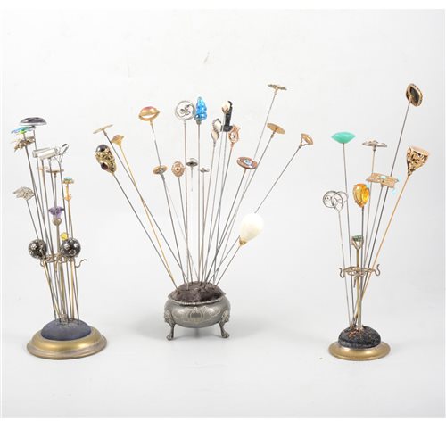 Lot 191 - Three metal hat pin stands with hat pins - to include silver Charles Horner Art Nouveau style bead and wire, a blue and green enamelled pin hallmarked Birmingham 1908