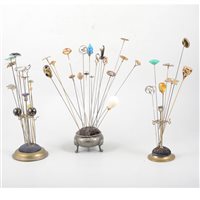 Lot 191 - Three metal hat pin stands with hat pins - to include silver Charles Horner Art Nouveau style bead and wire, a blue and green enamelled pin hallmarked Birmingham 1908
