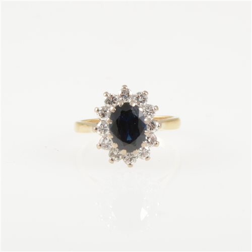 Lot 211 - A sapphire and diamond oval cluster ring, an oval mixed cut sapphire claw set and surrounded by twelve brilliant cut diamonds in an 18 carat yellow and white gold mount, hallmarked London 1976