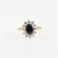 Lot 211 - A sapphire and diamond oval cluster ring, an oval mixed cut sapphire claw set and surrounded by twelve brilliant cut diamonds in an 18 carat yellow and white gold mount, hallmarked London 1976