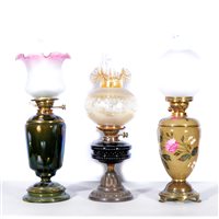 Lot 74 - Three oil lamps, to include Hink's Duplex, orange shade with impressed floral design, black ceramic reservoir with patterned beading decoration in different colours. (3)