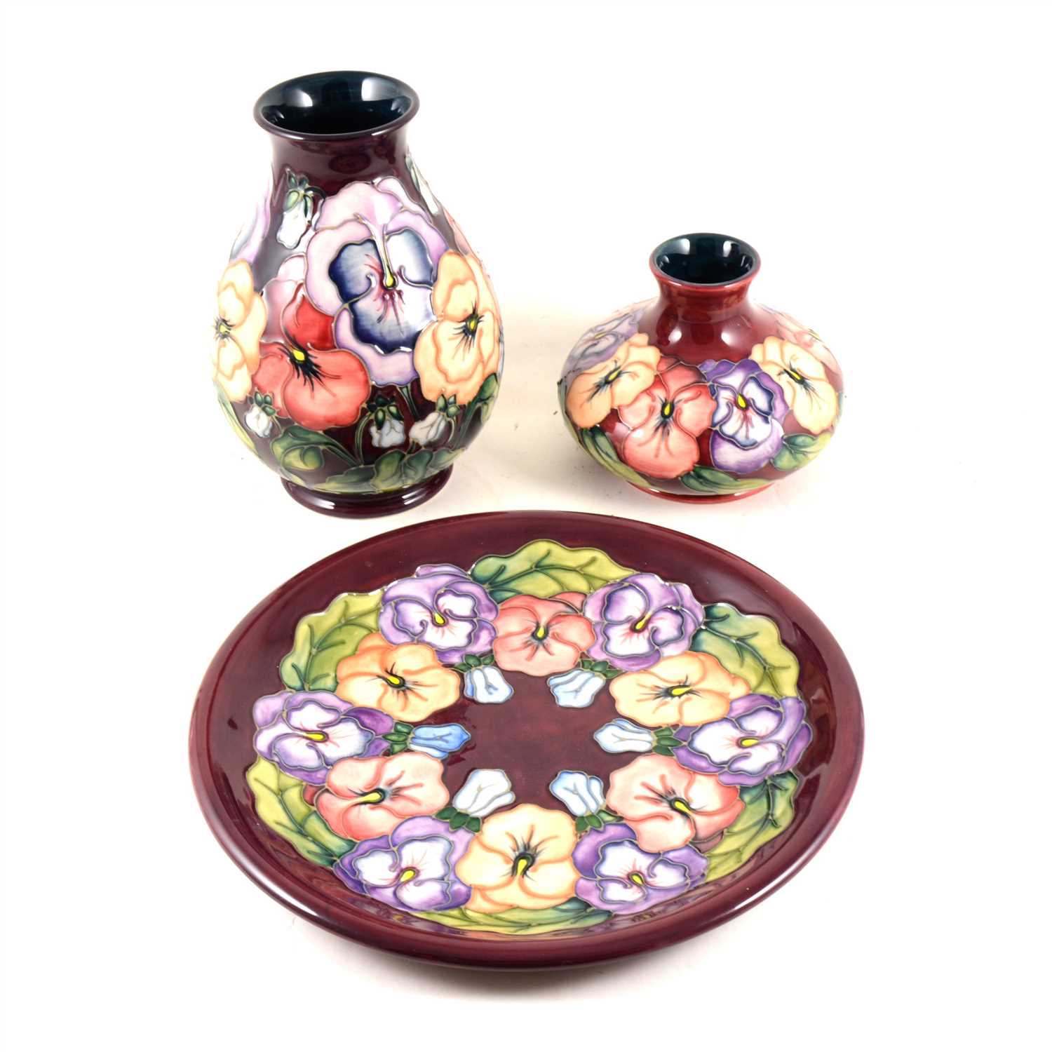 Lot 40 - A Moorcroft Pottery plate, "Pansy" designed by Rachel Bishop, 1994, 25.8cm diameter, and two vases of the same design and date, 11cm and 19cm.
