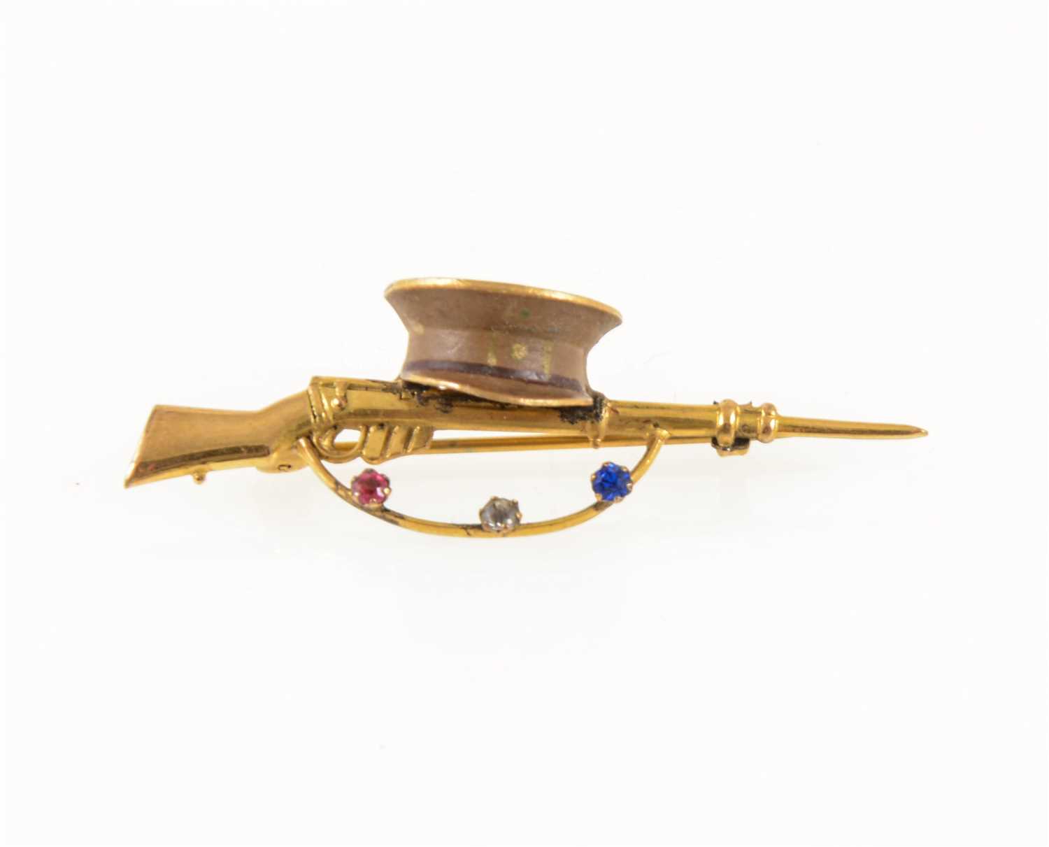 Lot 269 - A gold-plated bar brooch of military interest, a 50mm long rifle with cap and set with three paste stones, red, white and blue, Rd 641091.