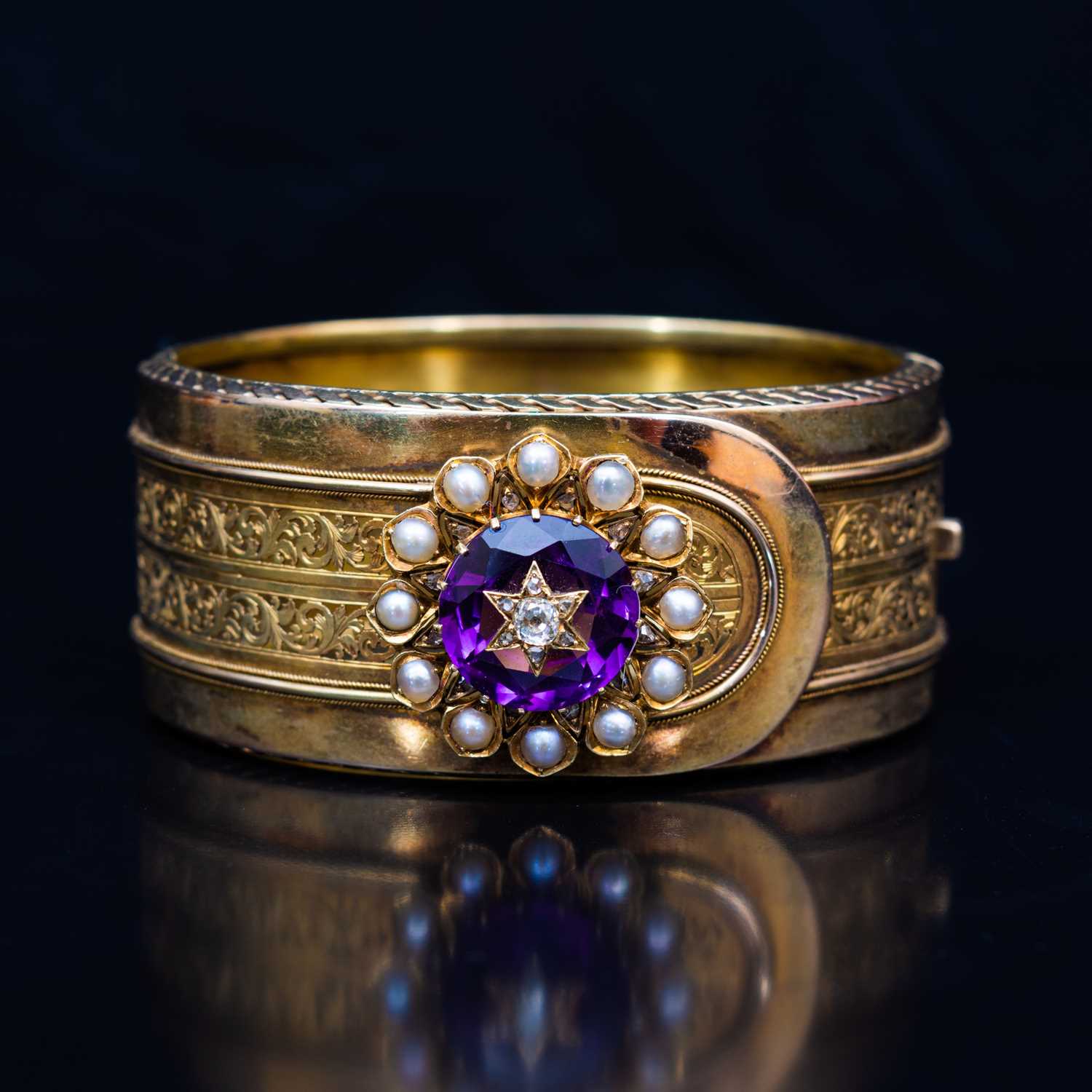 94 - A late 19th Century yellow metal bangle with an amethyst, diamond and pearl cluster.