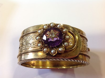 Lot 94 - A late 19th Century yellow metal bangle with an amethyst, diamond and pearl cluster.