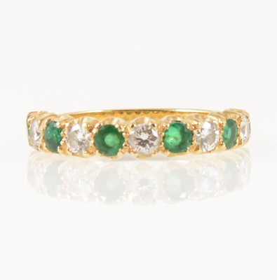 Lot 32 - An emerald and diamond half eternity ring.