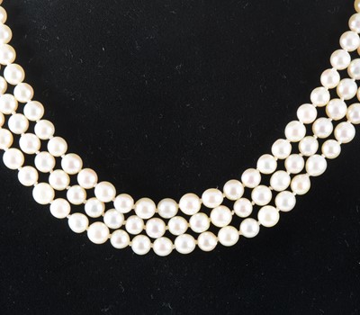 Lot 125 - A three row cultured pearl necklace with a diamond and emerald clasp.