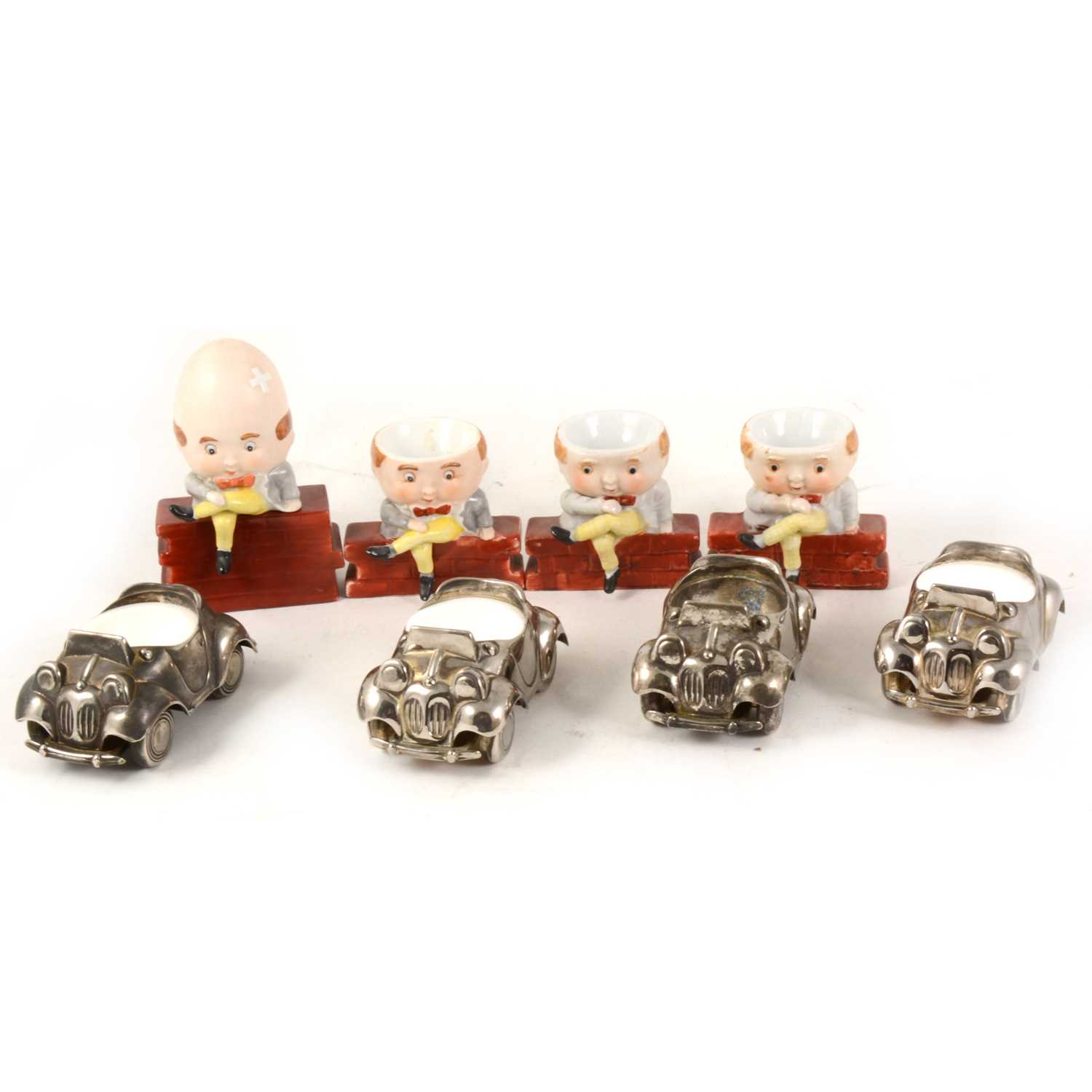 Lot 1026 - Three novelty porcelain Humpty Dumpty egg cups, and  four silver plated Noddy Car egg cups
