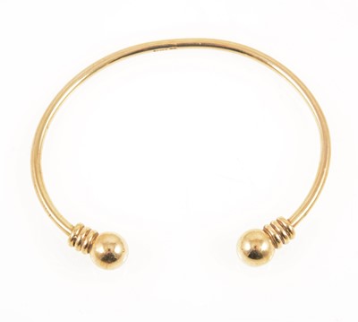 Lot 1300 - A 9 carat yellow gold torque style bangle with bead terminations.