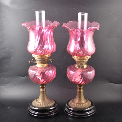 Lot 24 - A pair of cranberry glass oil lamps with fluted shades and reservoirs.
