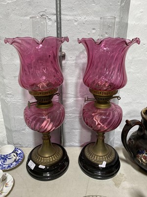 Lot 24 - A pair of cranberry glass oil lamps with fluted shades and reservoirs.