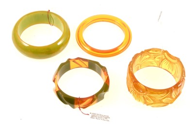 Lot 388 - Two "apple juice" lucite bangles and another similar slave bangle, bakelite bangle.