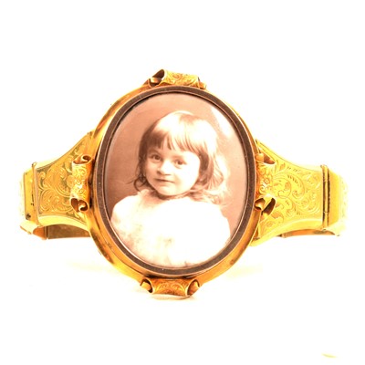 Lot 230 - A yellow metal bangle with photograph locket centre.